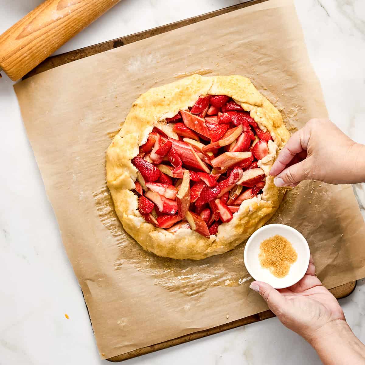 Woman sprinkling turbinado sugar on the crust of a galette.