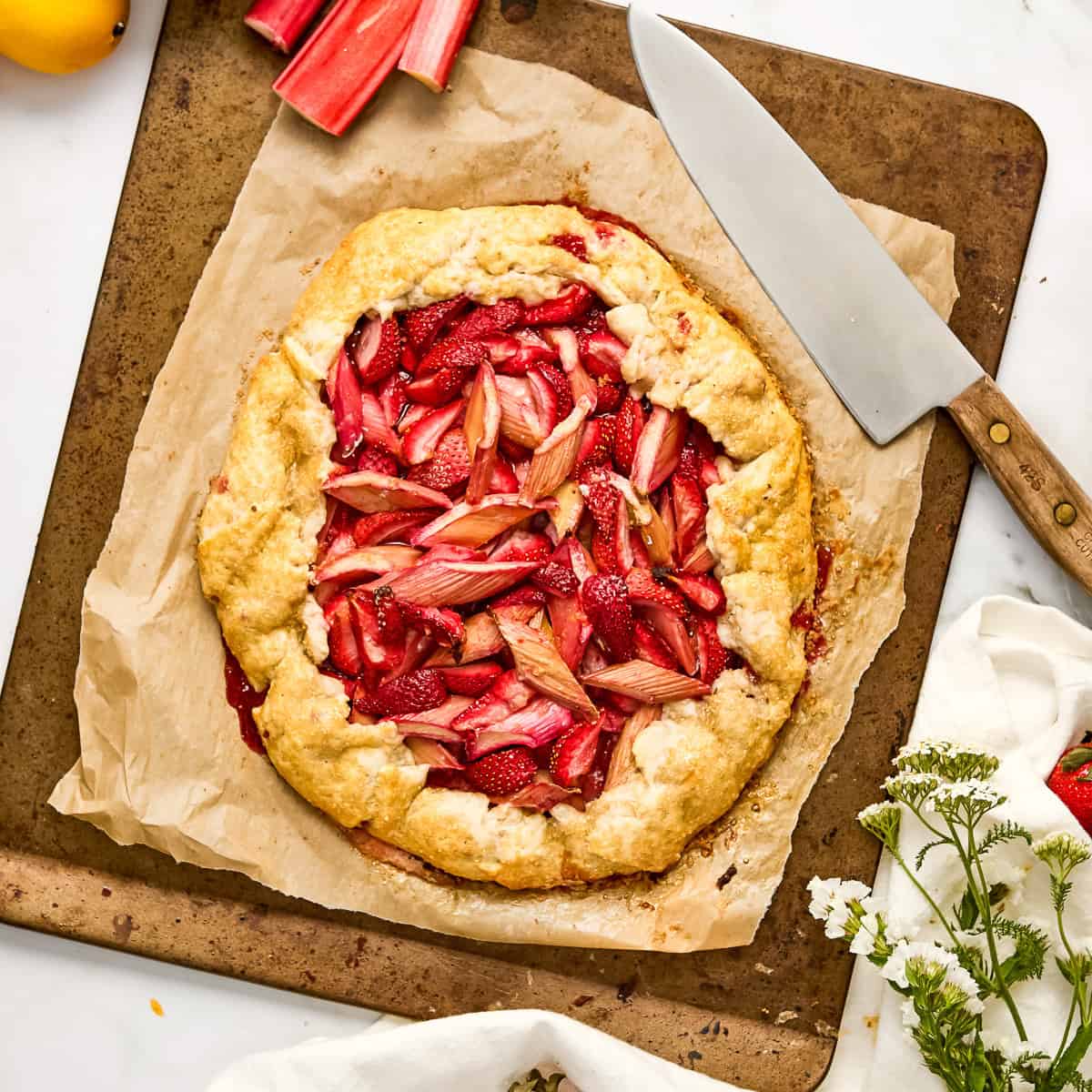 Rhubarb strawberry galette on a baking sheet after coming out of the oven next to knife.