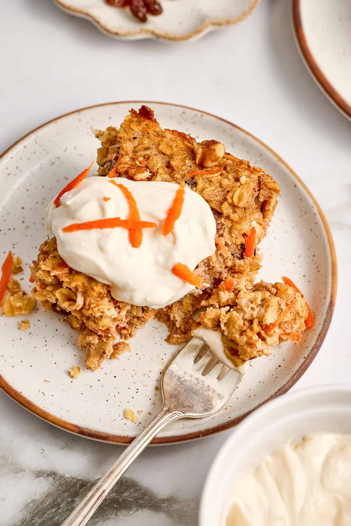 Carrot oatmeal with frosting and shredded carrots on a plate with a fork with a bite.