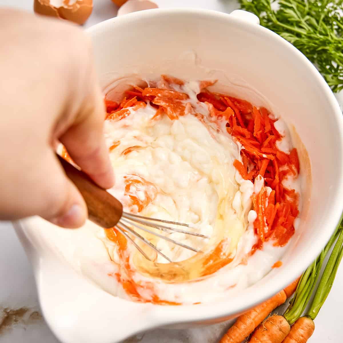 Woman whisking wet ingredients and shredded carrots for baked oatmeal.