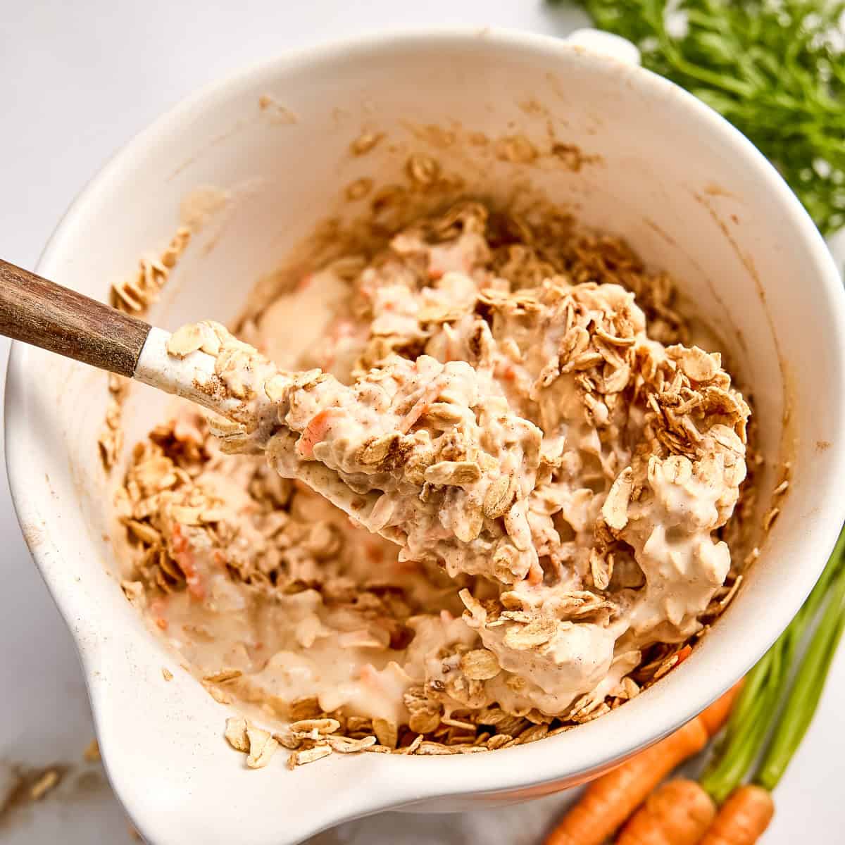 Woman stirring oats into wet ingredients in a bowl with a rubber spatula.
