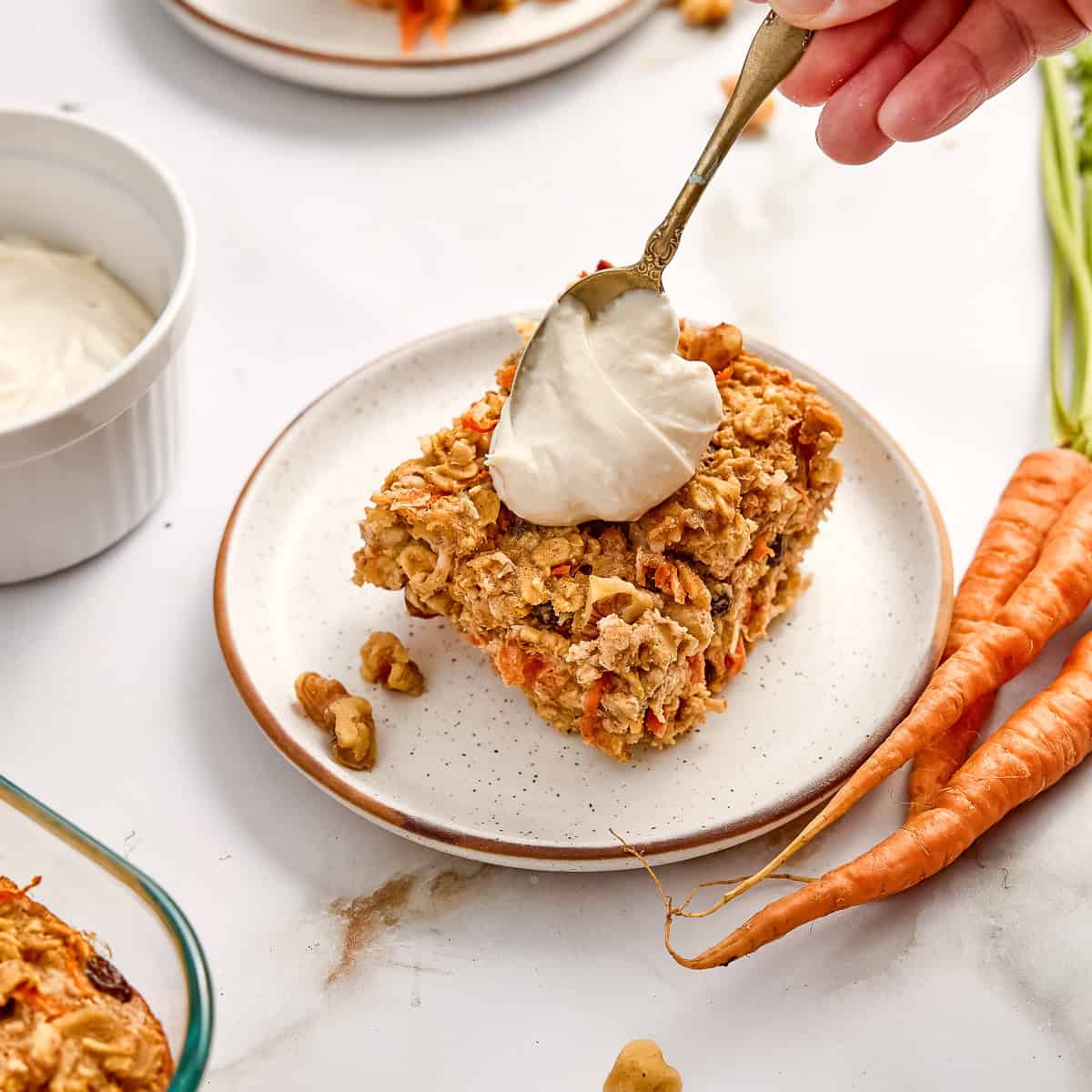 Woman spooning a dollop of cream cheese frosting on a slice of oatmeal.