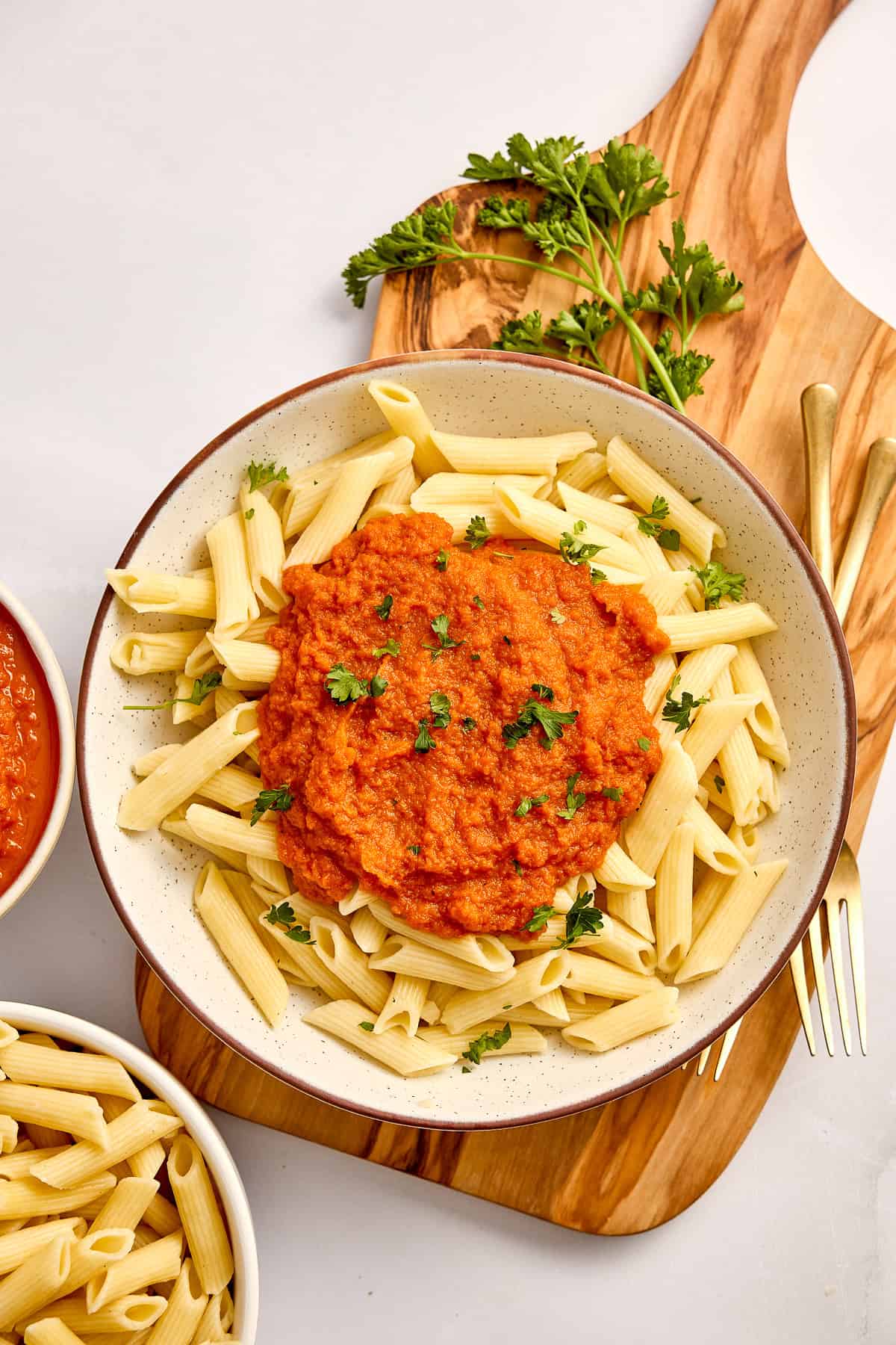 Penne pasta with carrot sauce in a bowl on a wooden board with forks and parsley.