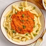 Bowl of penne pasta topped with carrot pasta sauce and fresh parsley next to forks.