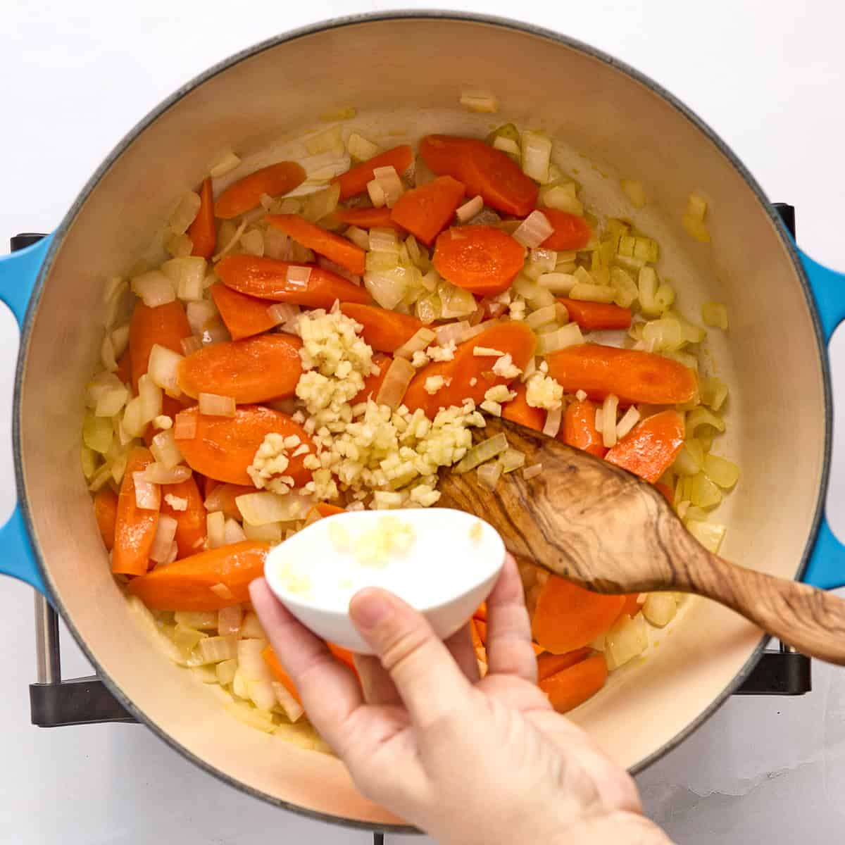 Woman adding minced garlic to a pot with cooked carrots and onions.