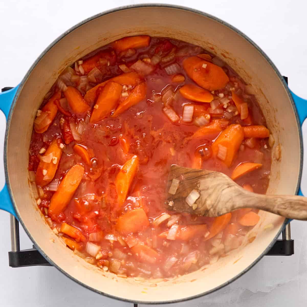 Carrot pasta sauce ingredients simmering in a large pot with a wooden spoon.