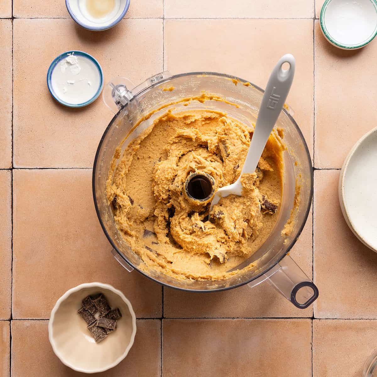 Chocolate chunks mixed into chickpea blondie batter in a food processor bowl.
