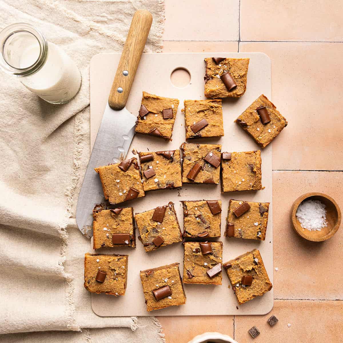 Blondies cut into sixteen squares on a cutting board next to a large knife.