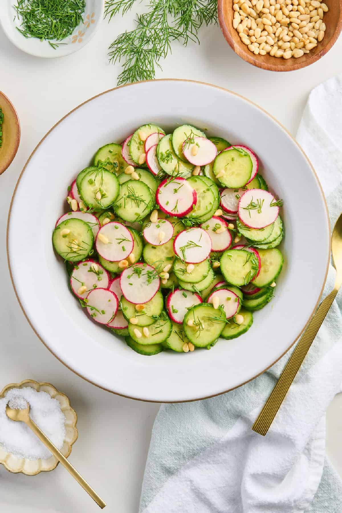 Cucumber radish salad in a bowl surrounded by ingredients, napkin, and spoon.