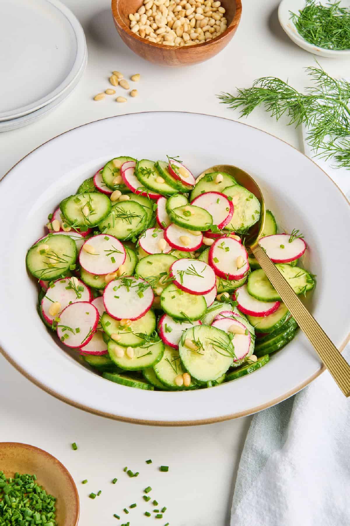 Cucumber and radish salad with lemon dressing in a bowl with gold spoon.