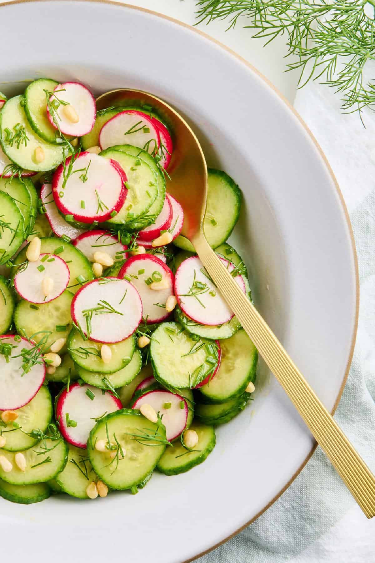 Thinly sliced radishes and cucumbers in a bowl with a gold spoon.