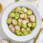 Cucumber radish salad in a bowl surrounded by ingredients, napkin, and spoon.