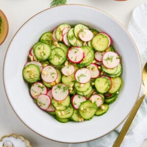 Cucumber radish salad in a bowl surrounded by ingredients, napkin, and spoon.