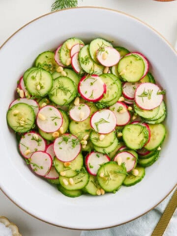 Cucumber radish salad in a bowl surrounded by ingredients, napkin, and spoon.