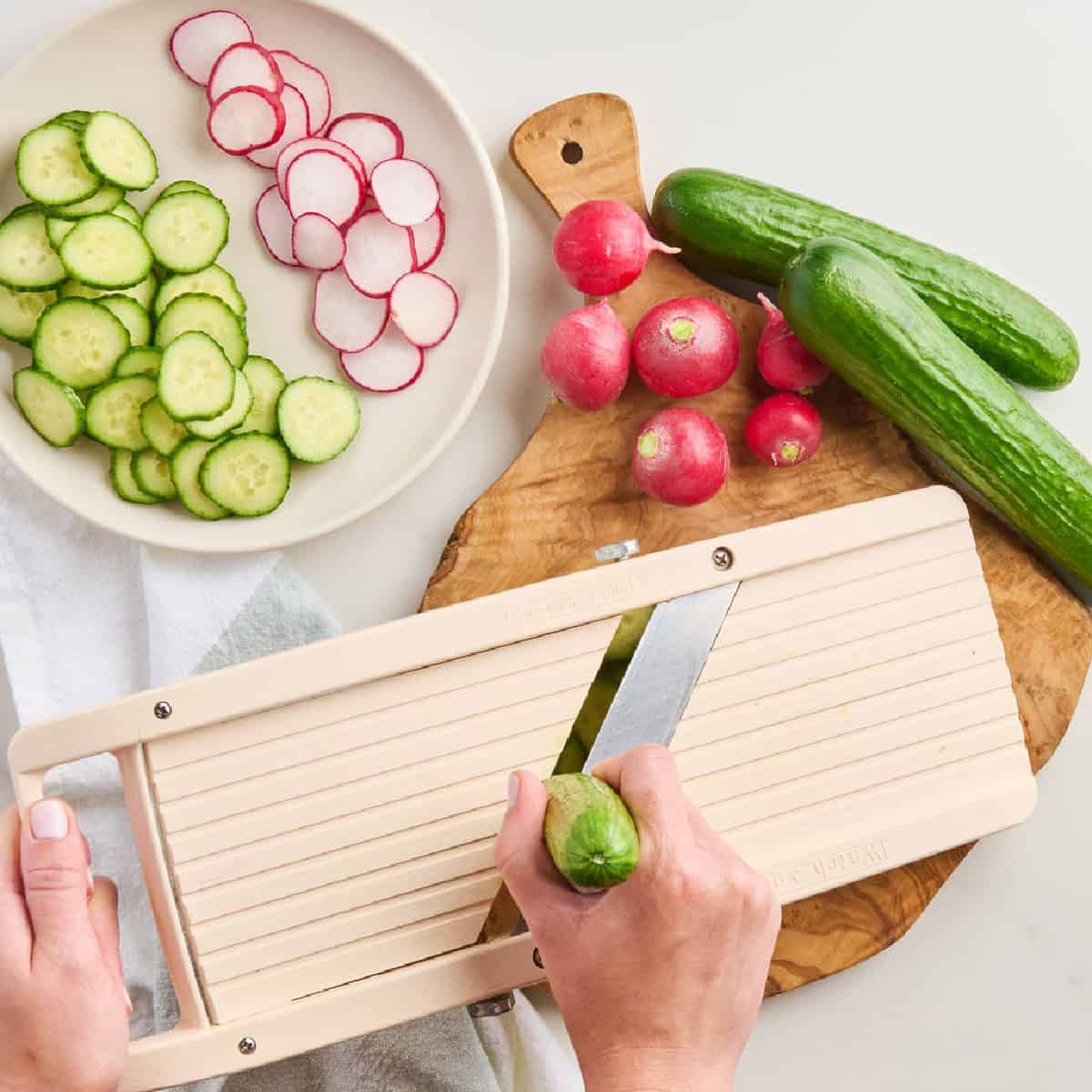 Woman slicing cucumbers with a mandoline over a cutting board.