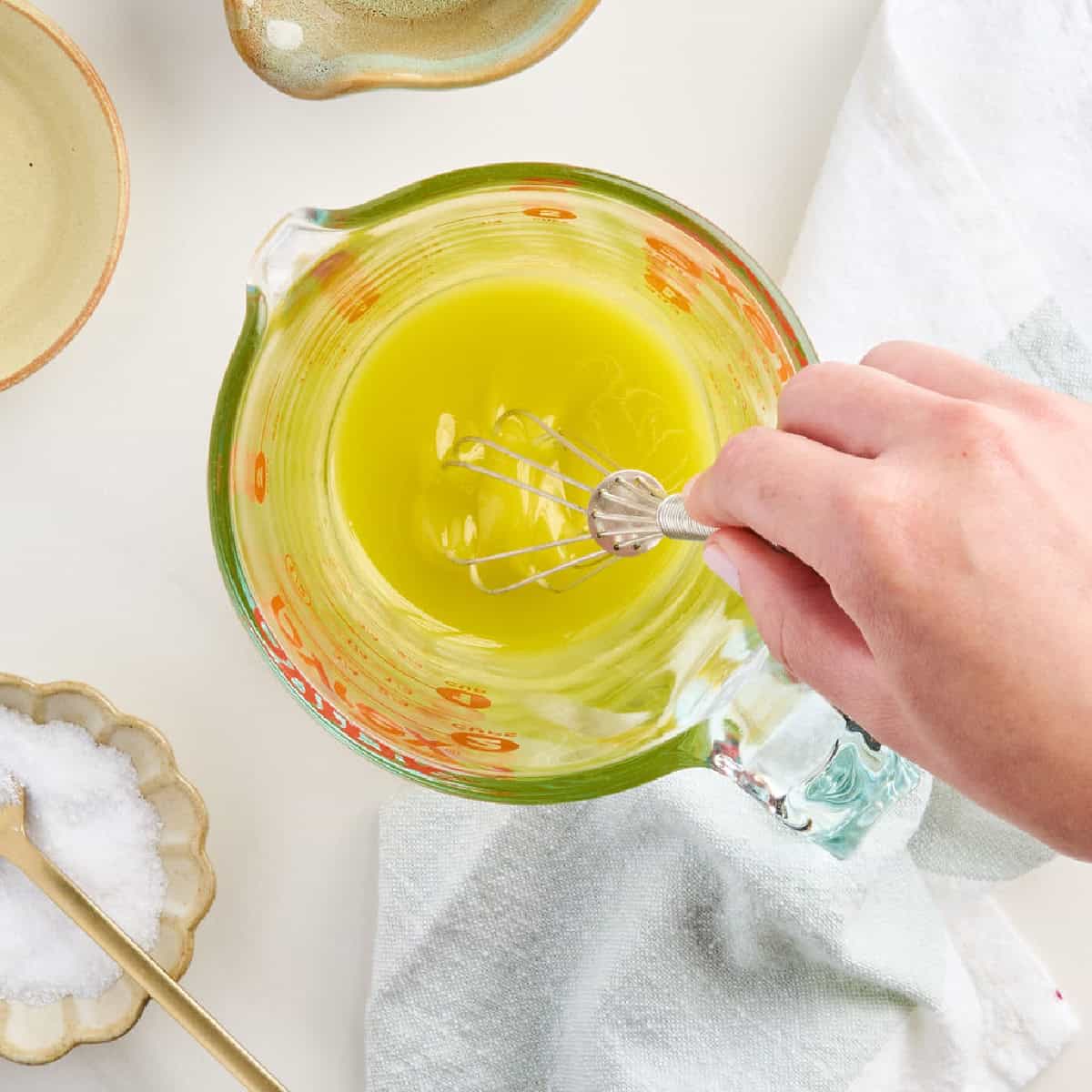 Woman whisking simple lemon olive oil dressing in a measuring cup.