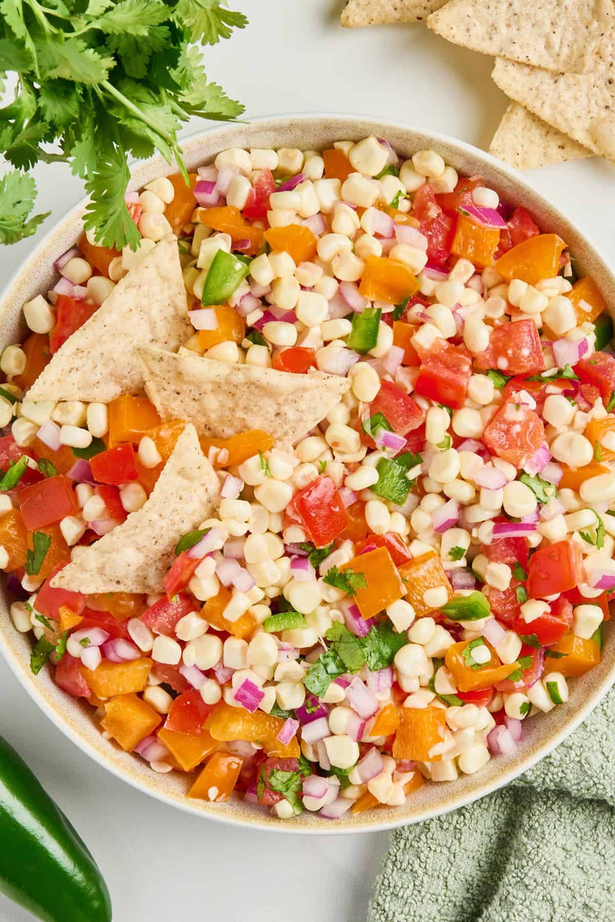 Corn salsa in a serving bowl with three tortilla chips sticking out of it.
