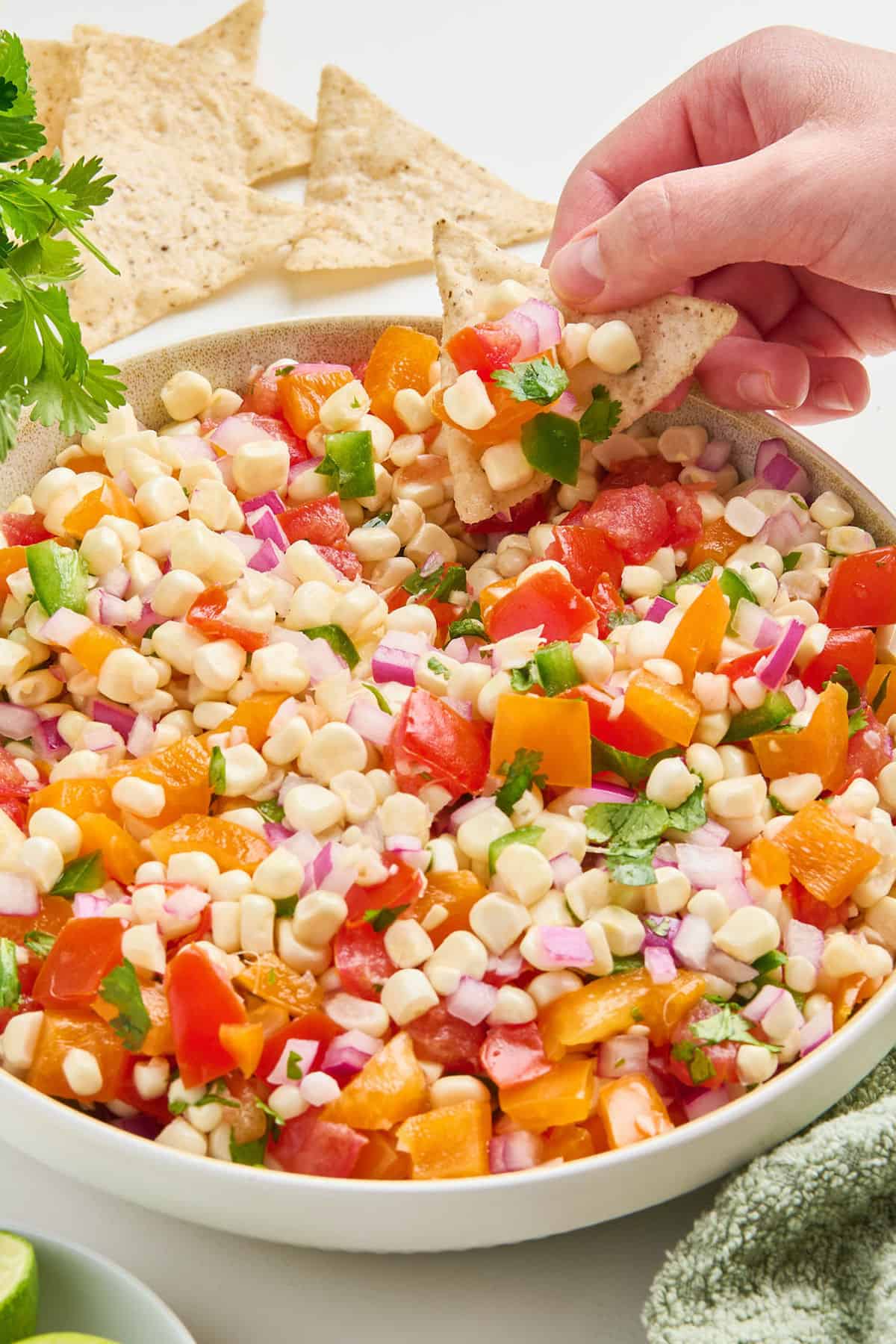Woman scooping up corn and tomato salsa with a tortilla chip in a large bowl.