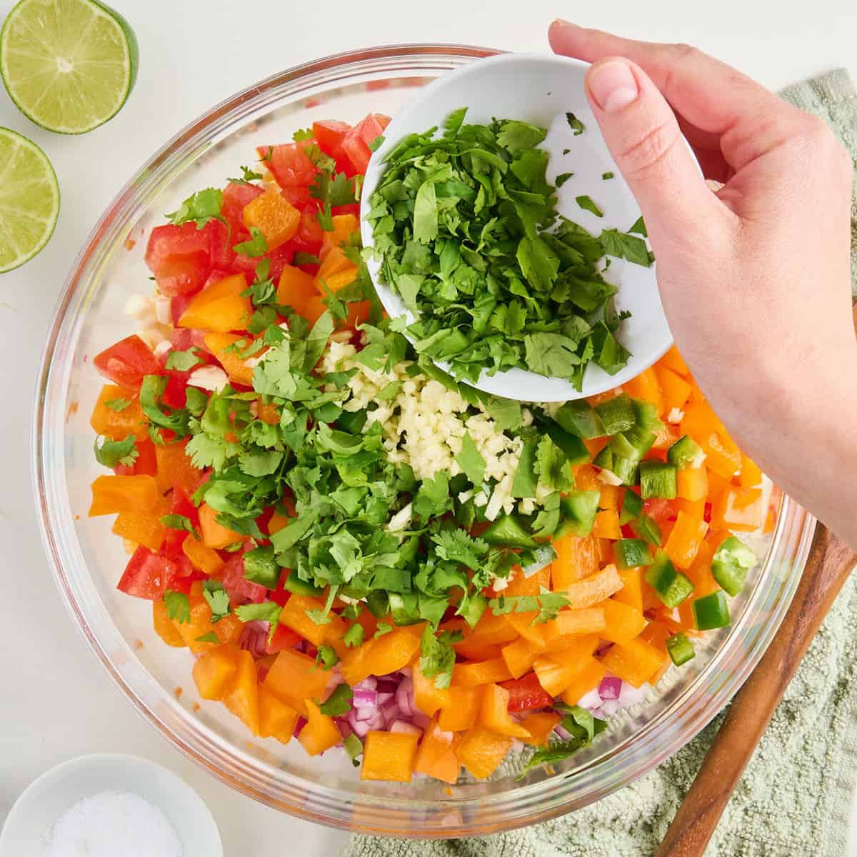 Woman pouring chopped cilantro into a bowl with other fresh corn salsa ingredients.