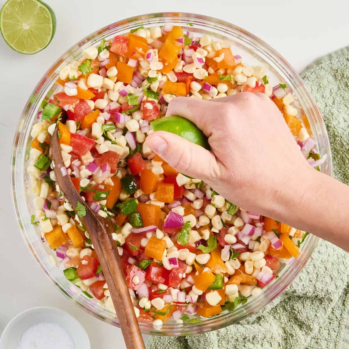 Woman squeezing a lime over salsa ingredients in a bowl with a wooden spoon.