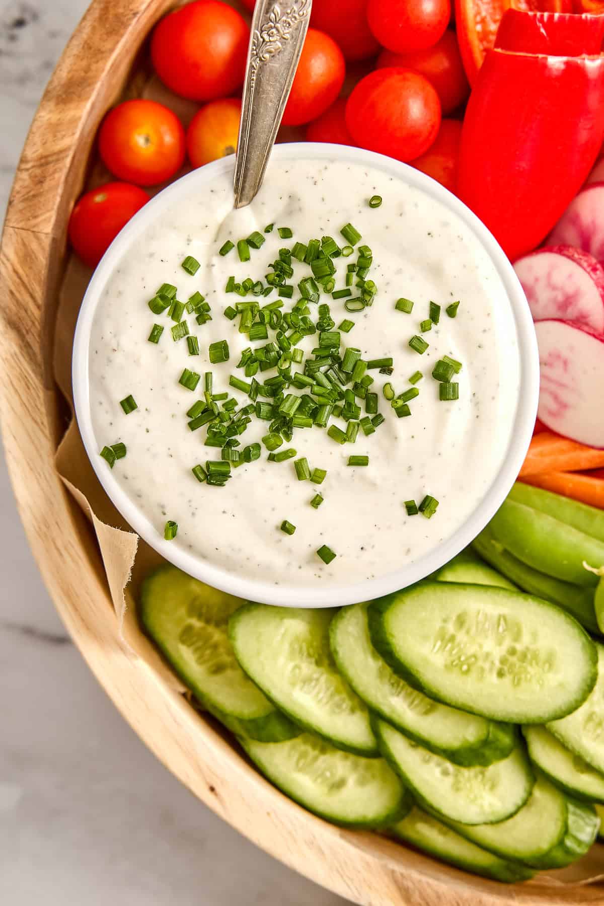 Creamy cottage cheese dip with chives in a bowl with a spoon on a veggie tray.