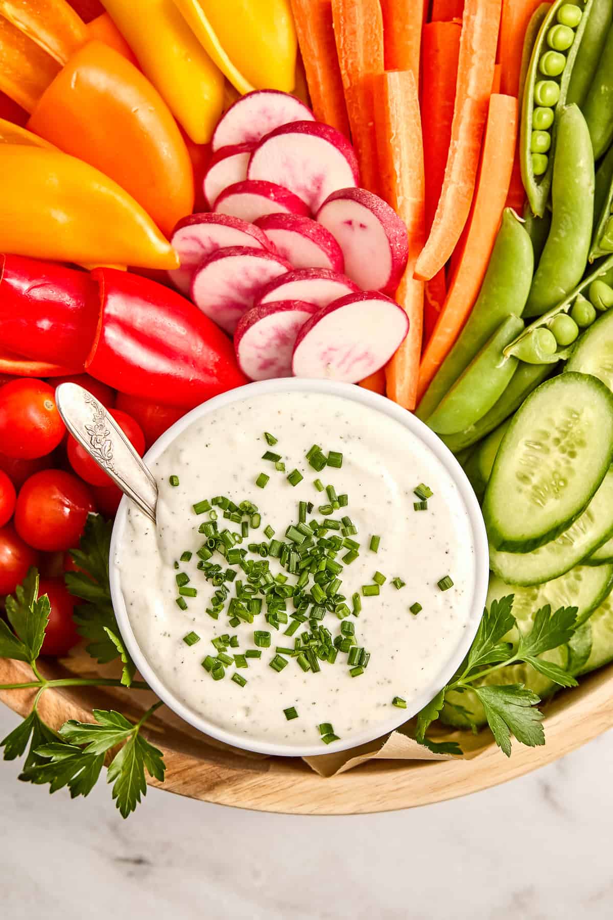 Baby peppers, radishes, carrots, snap peas, and cucumbers next to bowl of dip.