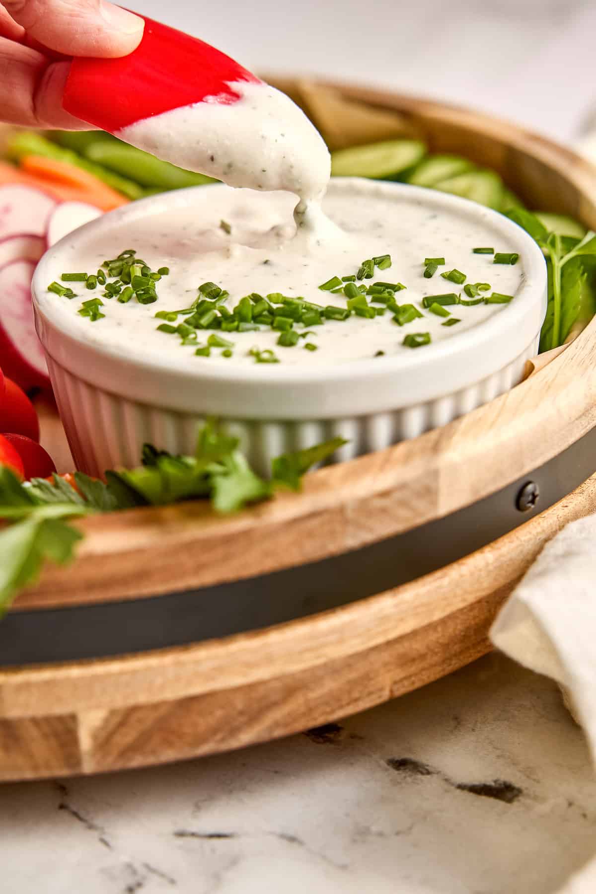 Woman dipping a red bell pepper in cottage cheese ranch dip with chives.