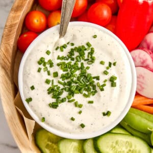 Creamy cottage cheese dip with chives in a bowl with a spoon on a veggie tray.