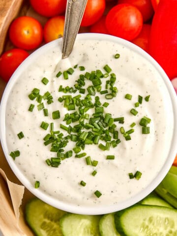 Creamy cottage cheese dip with chives in a bowl with a spoon on a veggie tray.