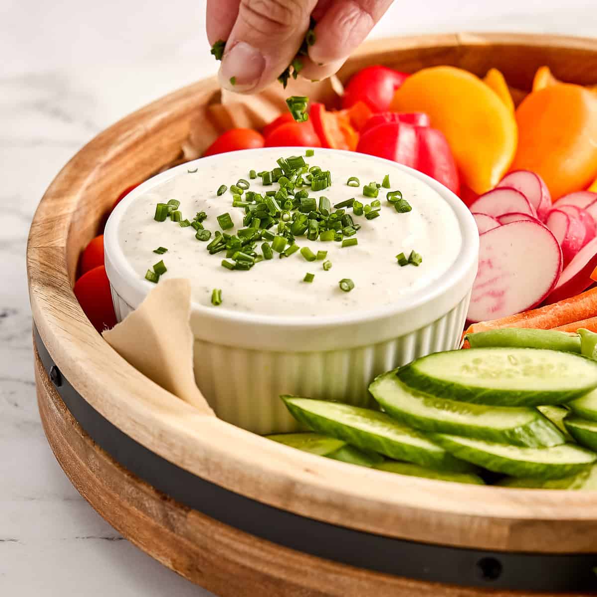 Woman sprinkling fresh chives on a bowl of veggie dip for a vegetable tray.