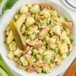 Dill pickle potato salad in a serving bowl next to ingredients, napkin, and plate with fork.