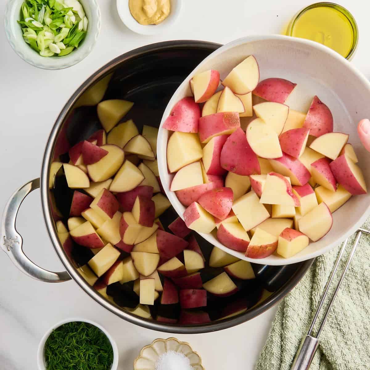 Chopped red potatoes being poured into a pot to be cooked for potato salad.