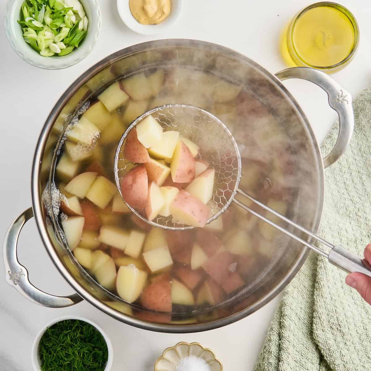 Cooked red potatoes in a wire skimmer over a pot of other potatoes.