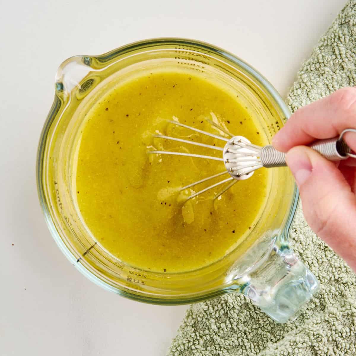 Woman whisking olive oil and dill pickle brine dressing in a measuring cup.