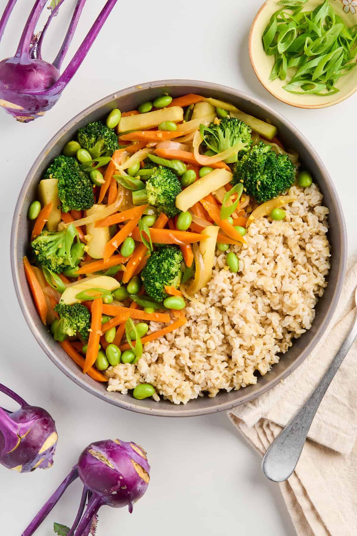 Kohlrabi stir fry served with brown rice in a plate surrounded by ingredients and napkin.