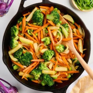 Vegetarian stir fry cooking in a cast iron skillet with a wooden spoon.
