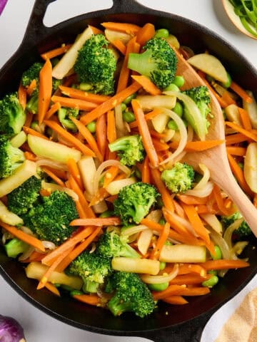 Vegetarian stir fry cooking in a cast iron skillet with a wooden spoon.