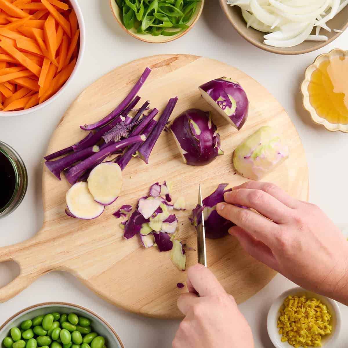 Woman peeling purple kohlrabi skin with a paring knife on a cutting board.