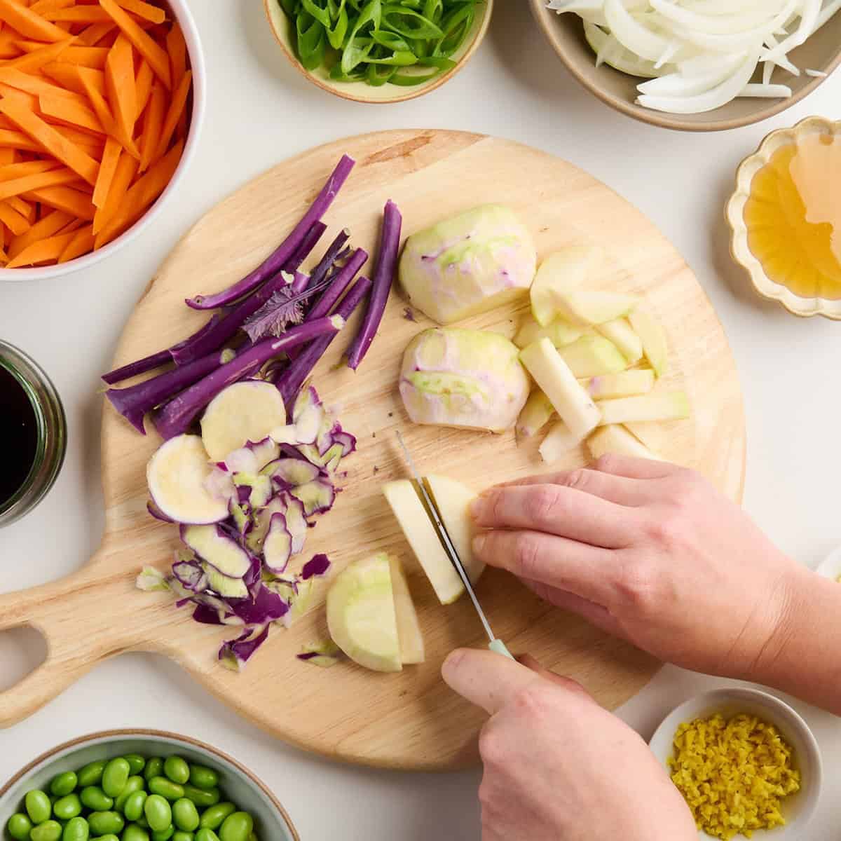 Woman cutting kohlrabi into strips for stir fry on a cutting board.