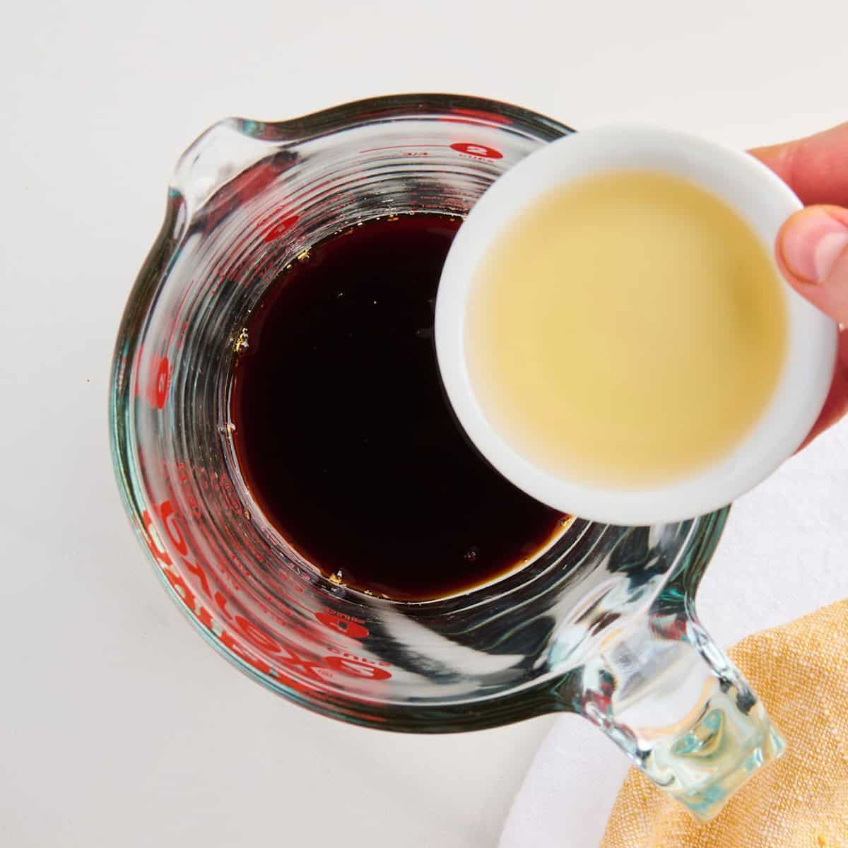 Woman adding rice vinegar to soy sauce, honey, garlic, and ginger in a measuring cup.