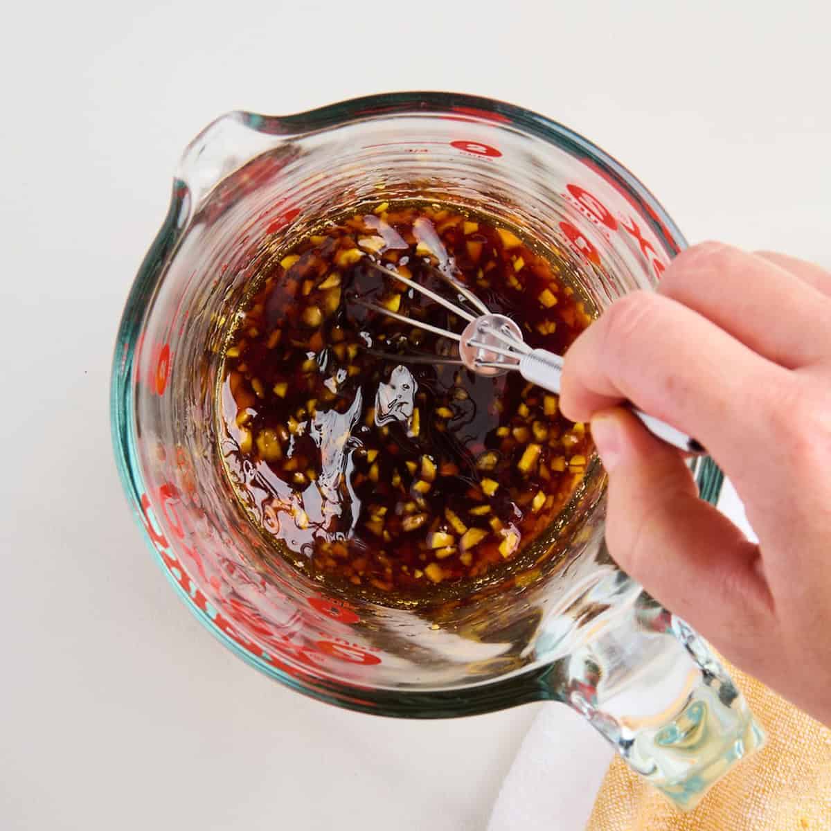 Woman whisking simple garlic ginger stir fry sauce in a measuring cup.