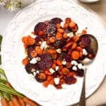 Roasted beets and carrots with goat cheese on a serving plate with silver spoon.