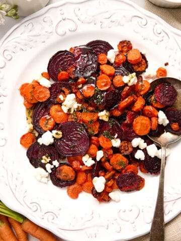 Roasted beets and carrots with goat cheese on a serving plate with silver spoon.