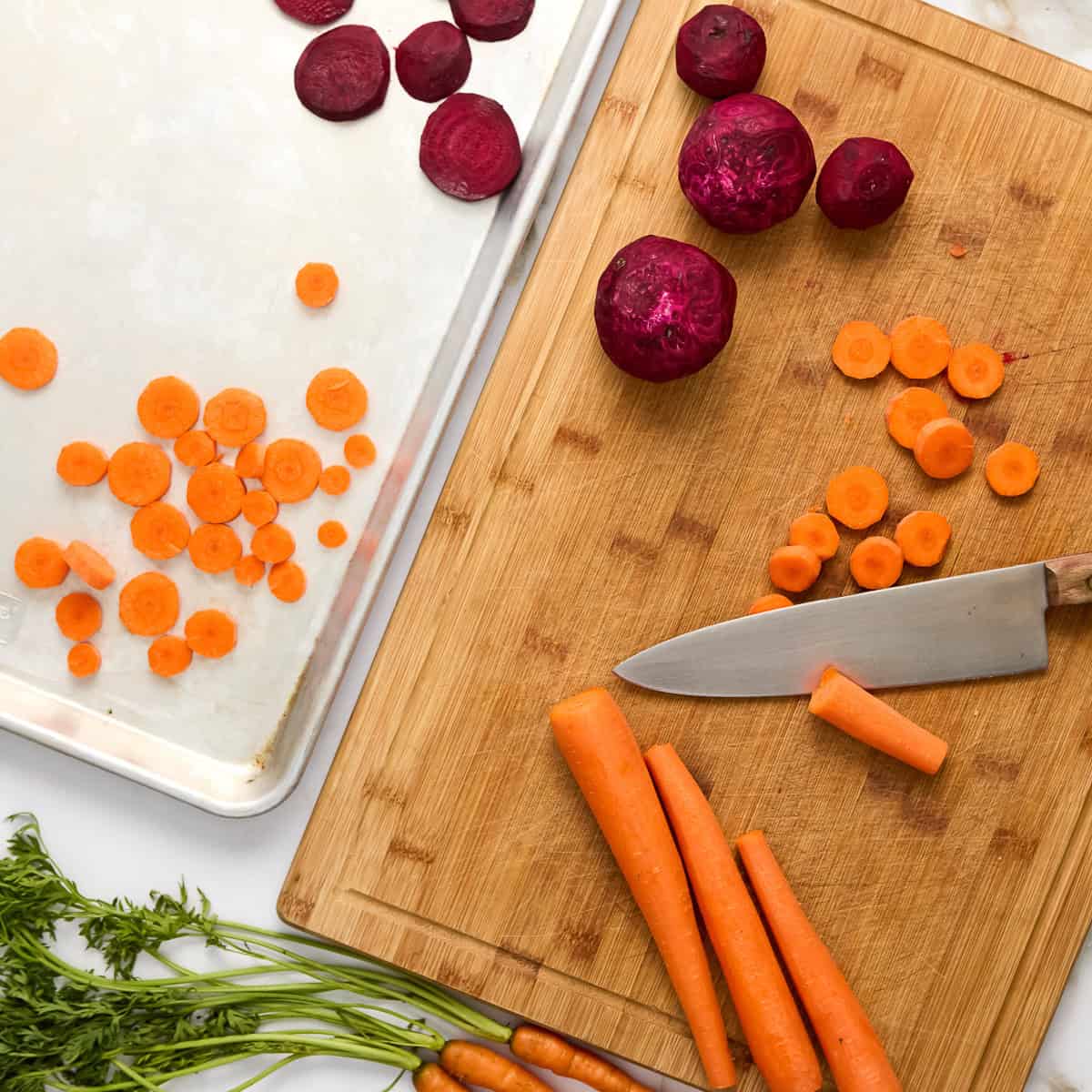 Carrots and beets being sliced on a cutting board and put onto a baking sheet.