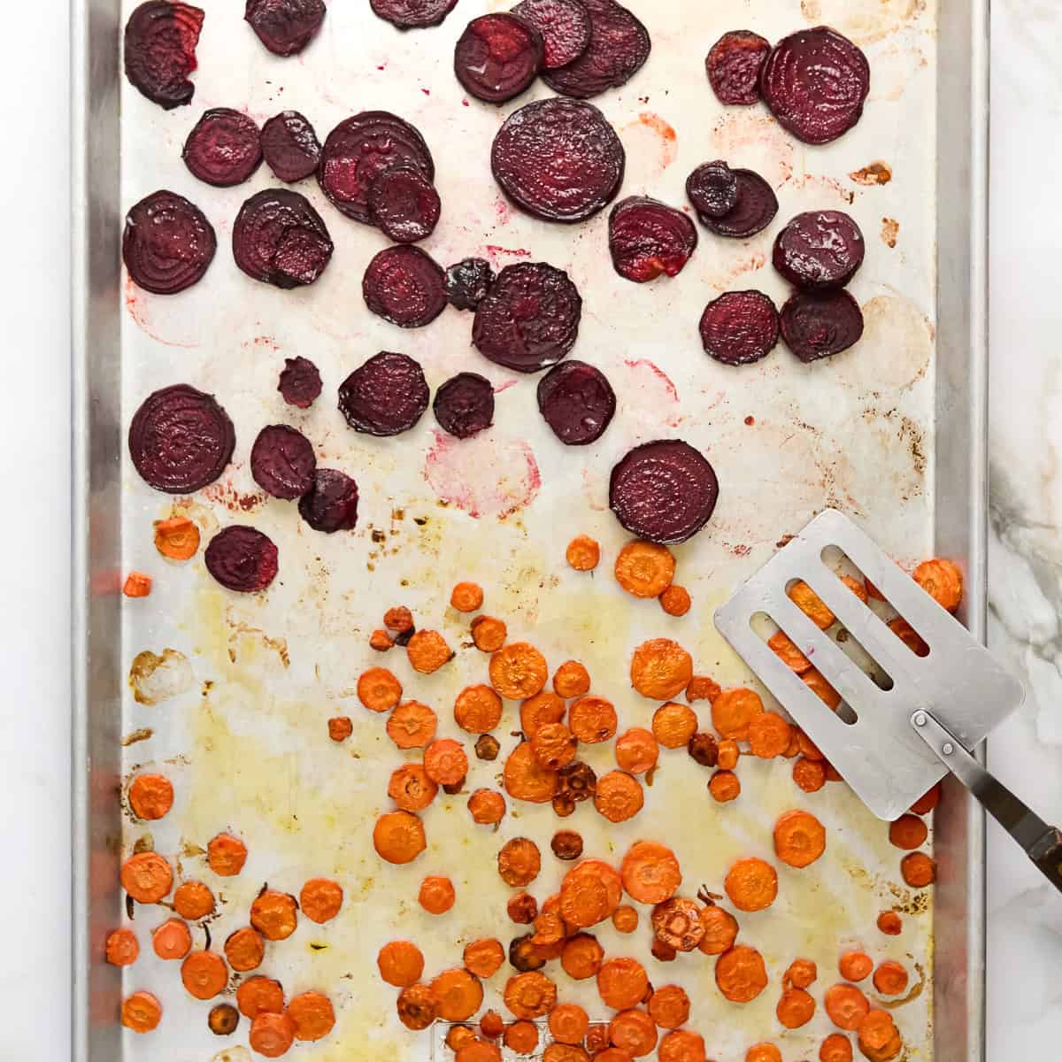 Roasted beets and carrots on a large baking sheet after coming out of the oven.