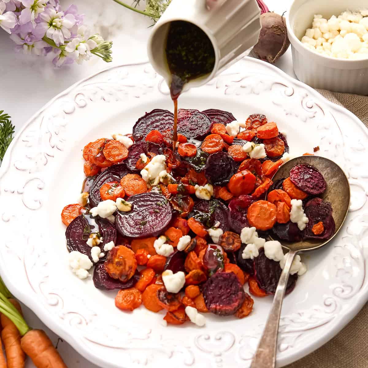 Balsamic glaze being poured over roasted veggies and goat cheese on a plate.