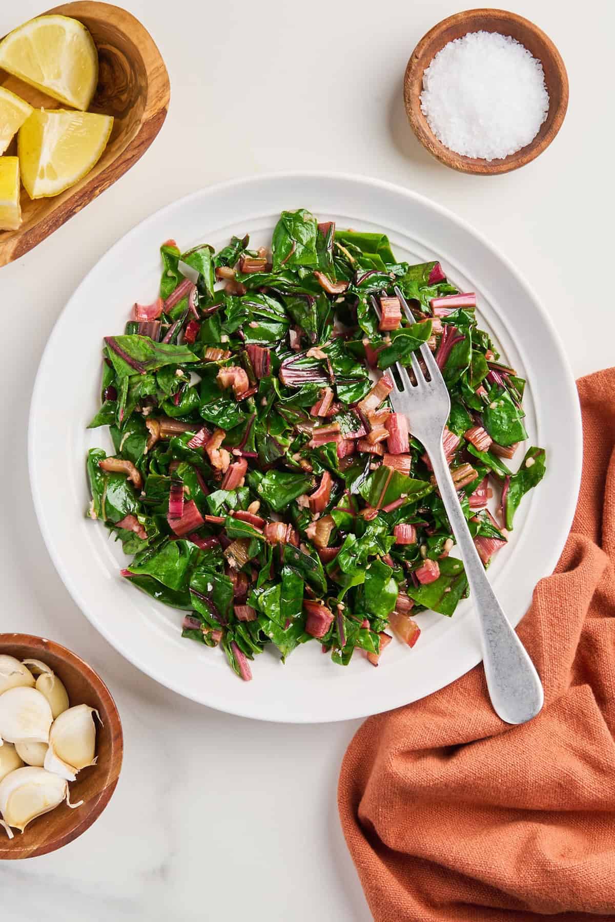 Sautéed red chard on a plate with a fork surrounded by ingredients and napkin.