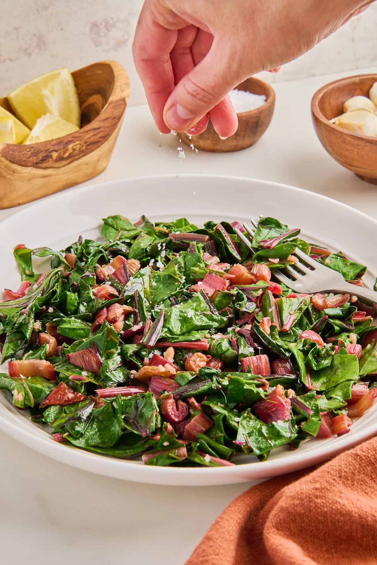 Woman sprinkling flaky salt on sautéed red chard on a serving plate.