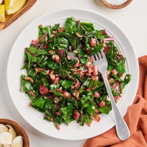 Sautéed red chard on a plate with a fork surrounded by ingredients and napkin.