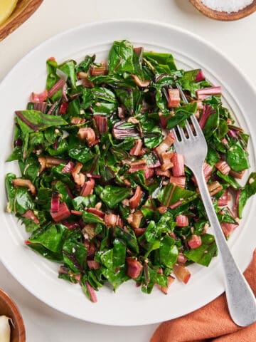 Sautéed red chard on a plate with a fork surrounded by ingredients and napkin.